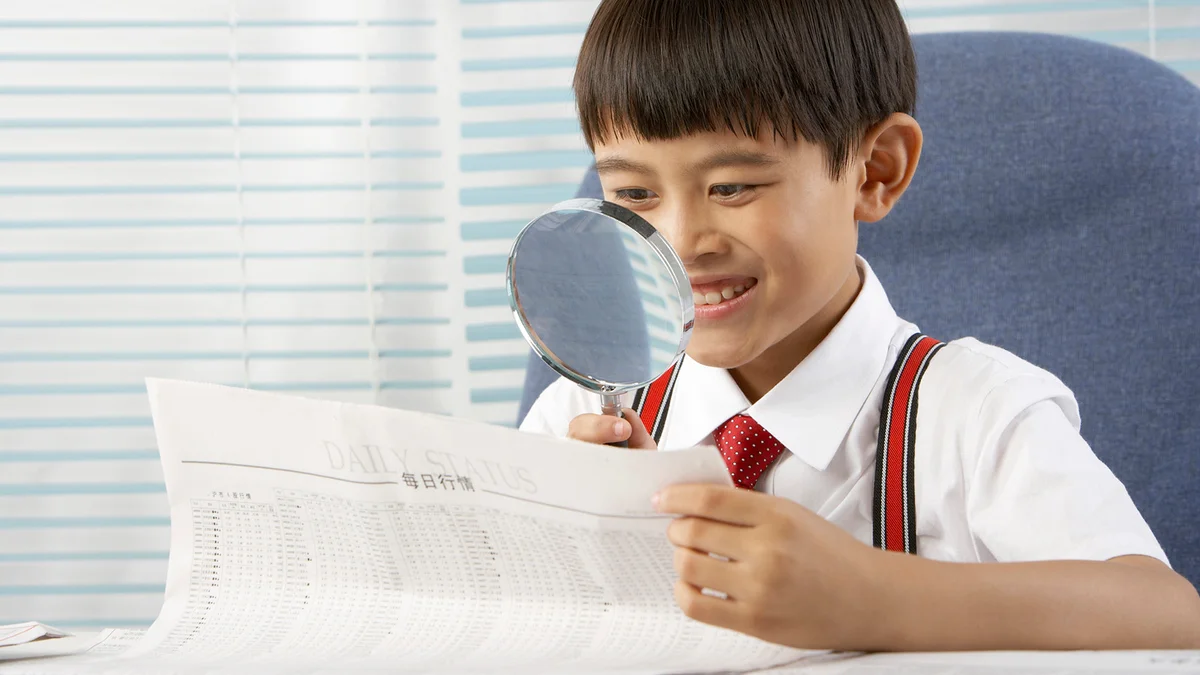 A boy reading newspaper with a magnifying glass