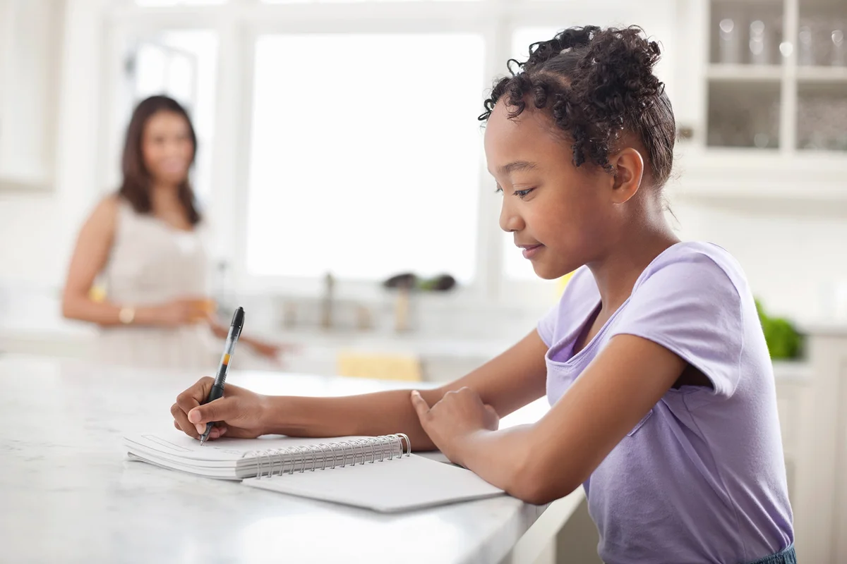 Girl writing food diary in kitchen