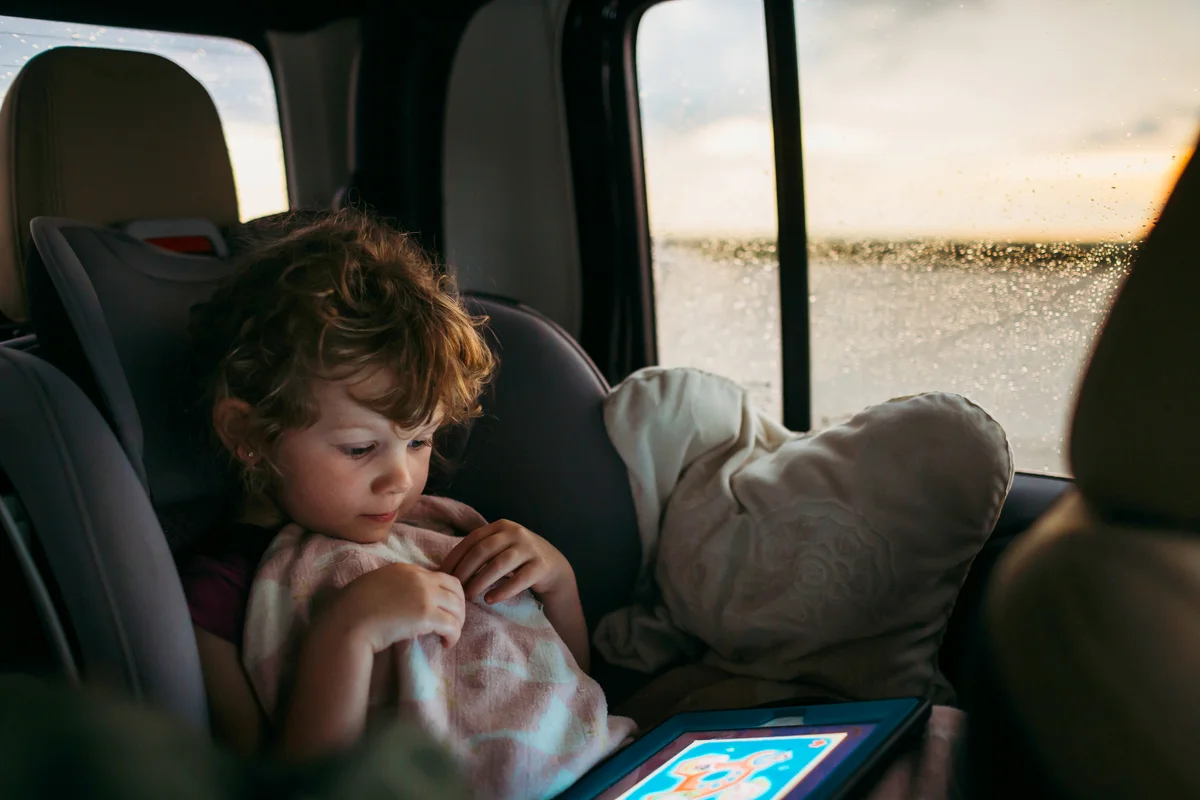 Young girl playing educational game on car ride home while it rains