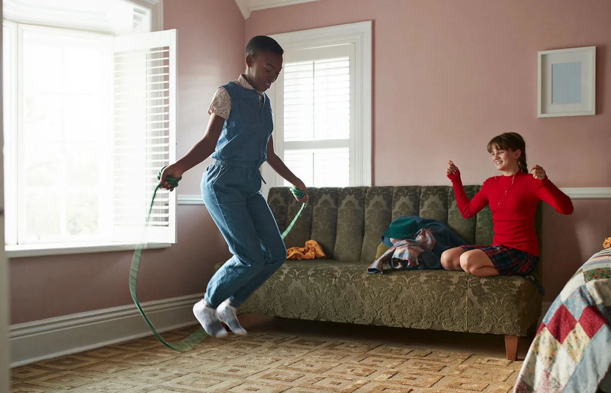 Girl skipping at home, while friend is cheering