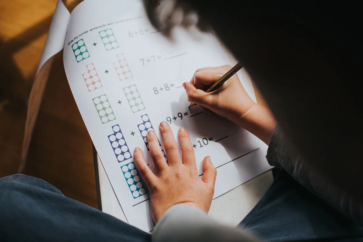 Child adding numbers on a printed maths sheet of homework