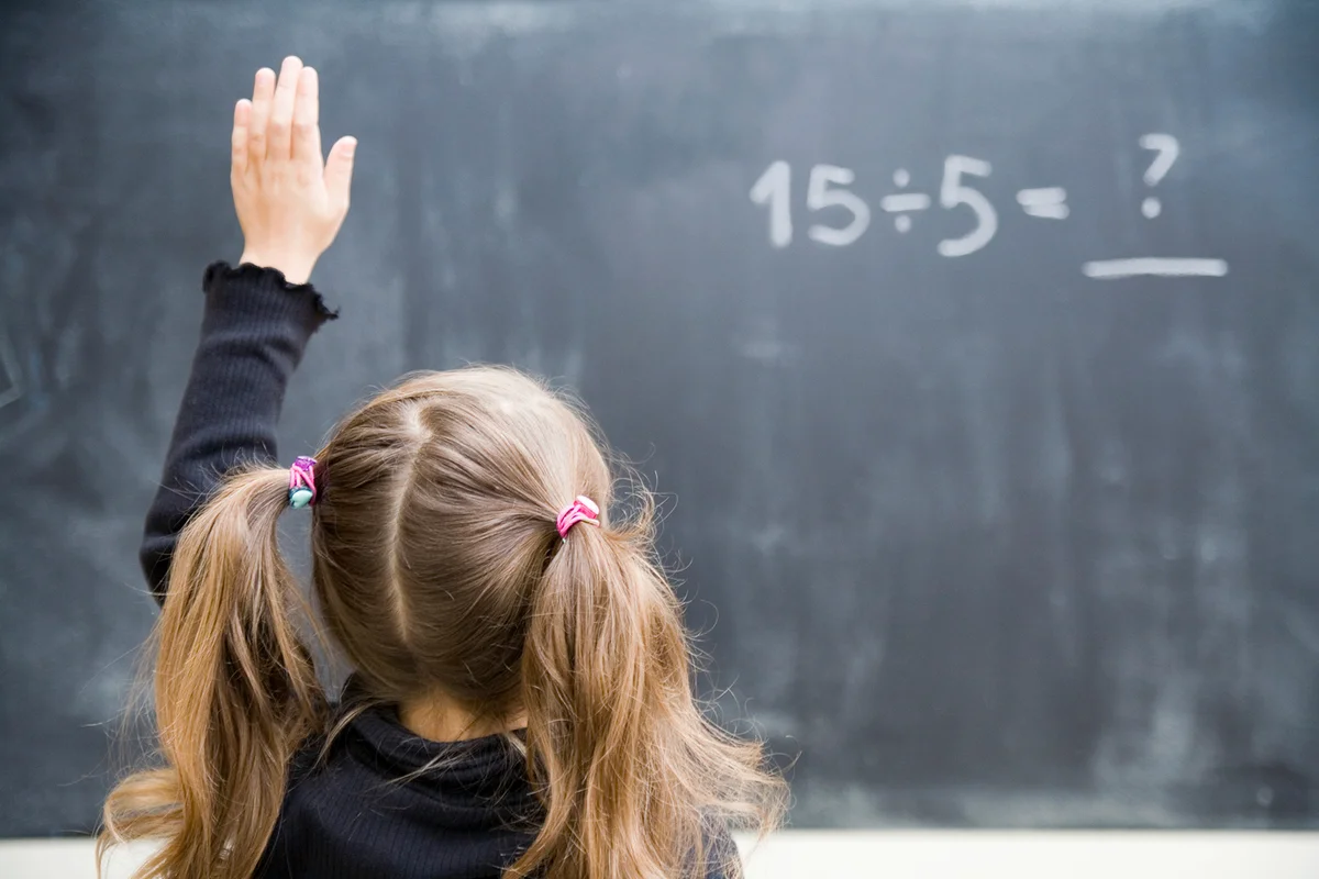 Girl in classroom with raised hand to answer a division