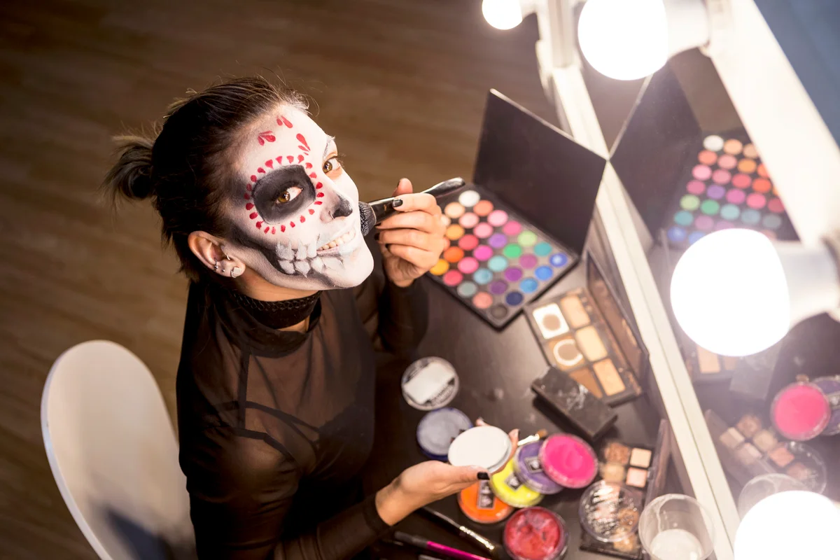 Woman painting face for Halloween night party looking at mirror getting ready looking at camera
