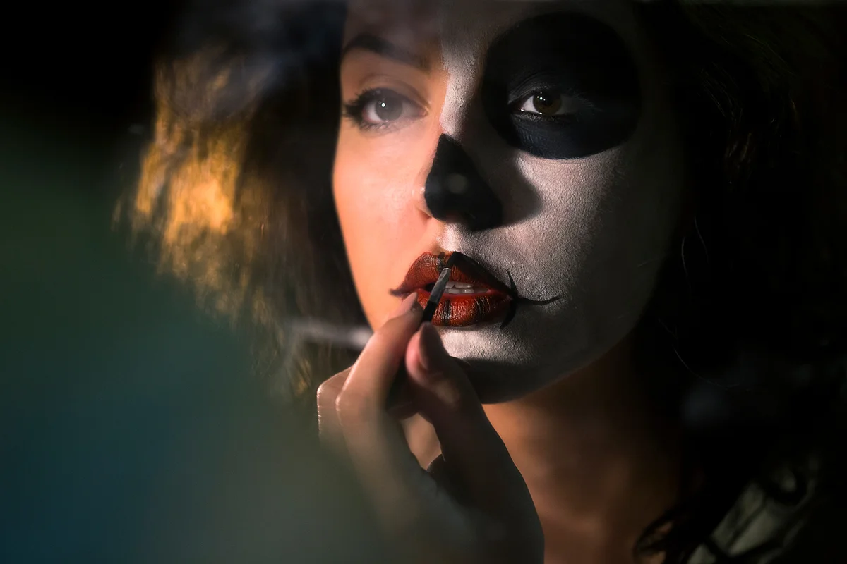 Woman painting make-up while looking in mirror behind a scene