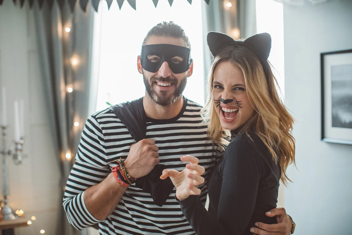 Couple at home party celebrating Halloween in costume of thief and cat-woman