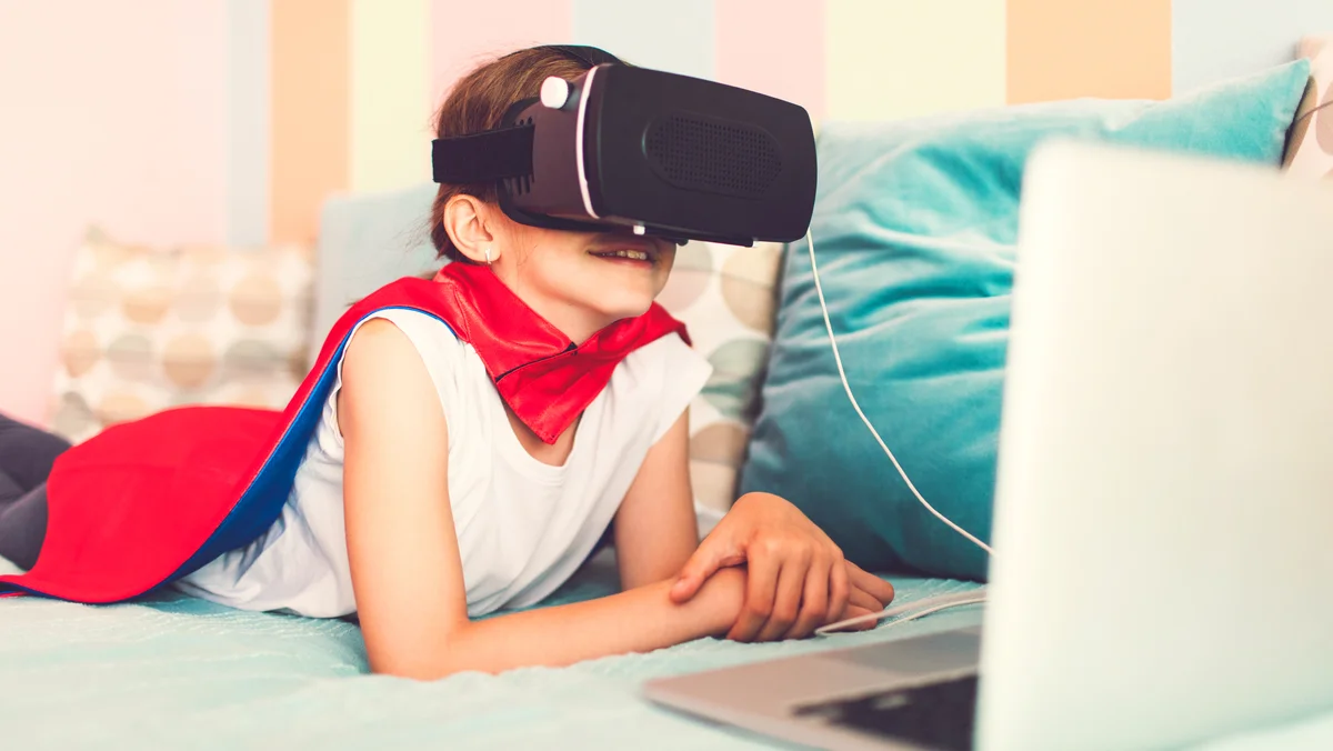Girl laying on the bed and wearing superhero cape playing video games