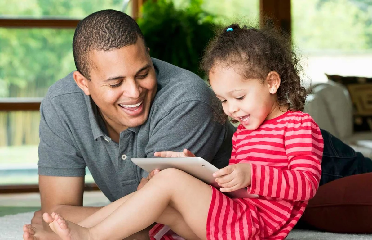 Father watching daughter using digital tablet on floor