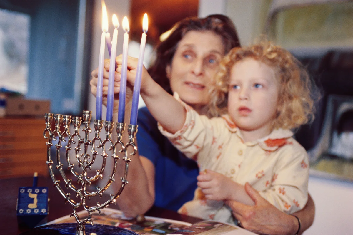 Grandmother helping granddaughter light Hanukkah candles