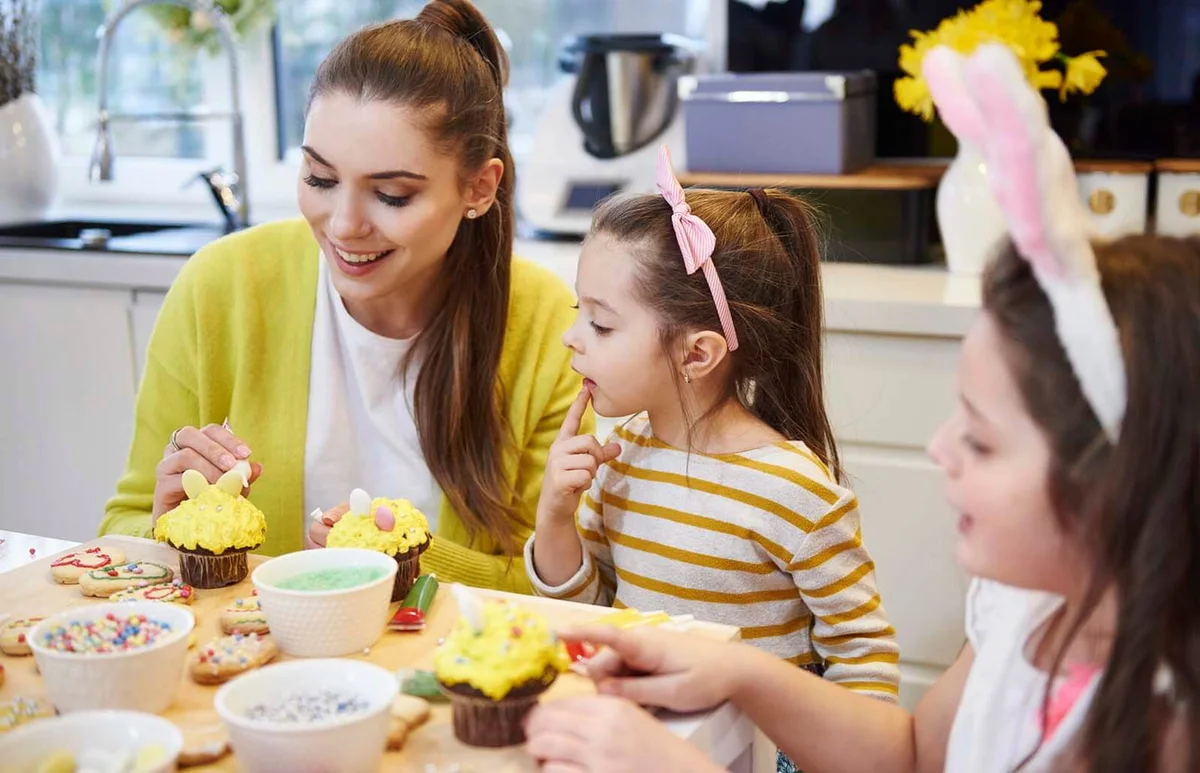 Mother with daughters decorating Easter cookies and muffins in kitchen