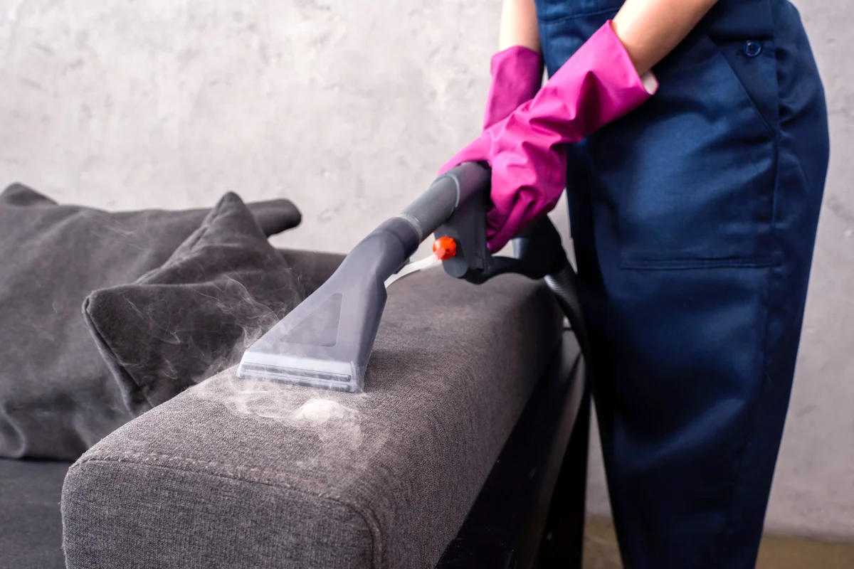 Woman using vacuum cleaner with hot steam on couch upholstery