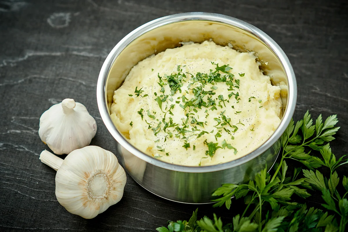 Creamy puree of potatoes sprinkled with parsley in a silver pot on a black table