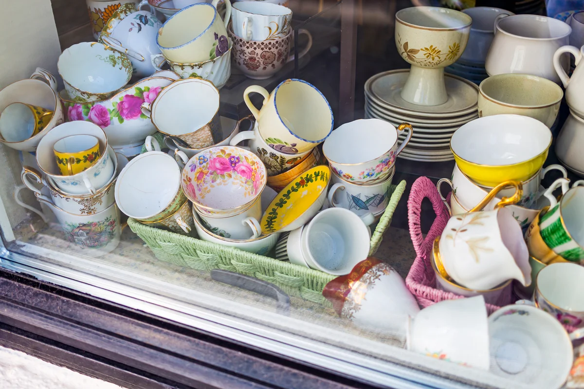 A variety of old teacups, saucers, jugs and other crockery items for sale in a second hand shop window