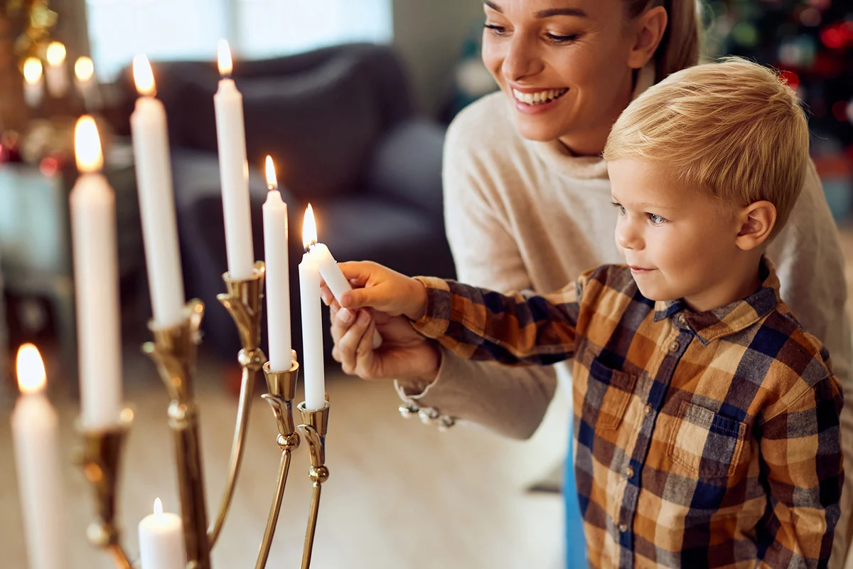 Jewish son and mother lighting the Menorah for Hanukkah at home