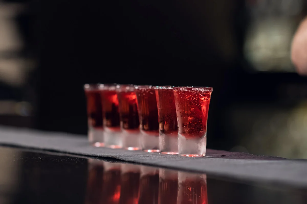 Bartender pours red alcohol into shots on the bar