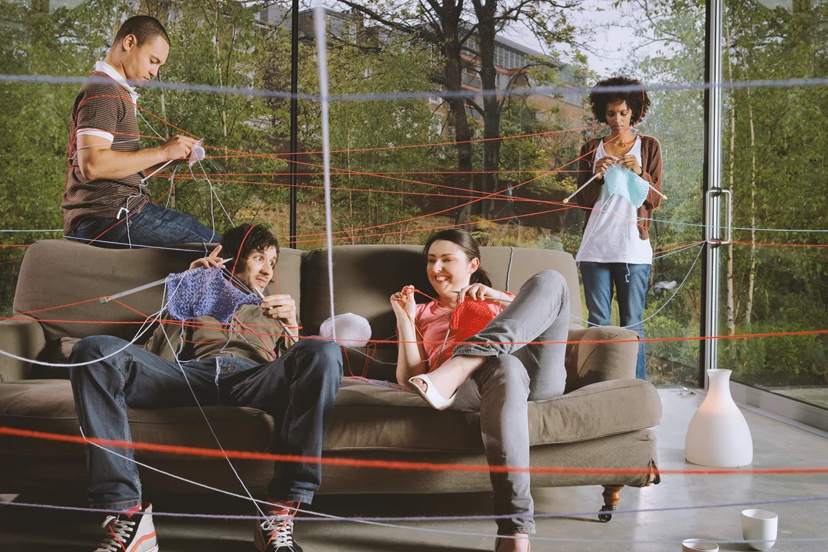 Group of young people knitting while being entangled in knitting tread