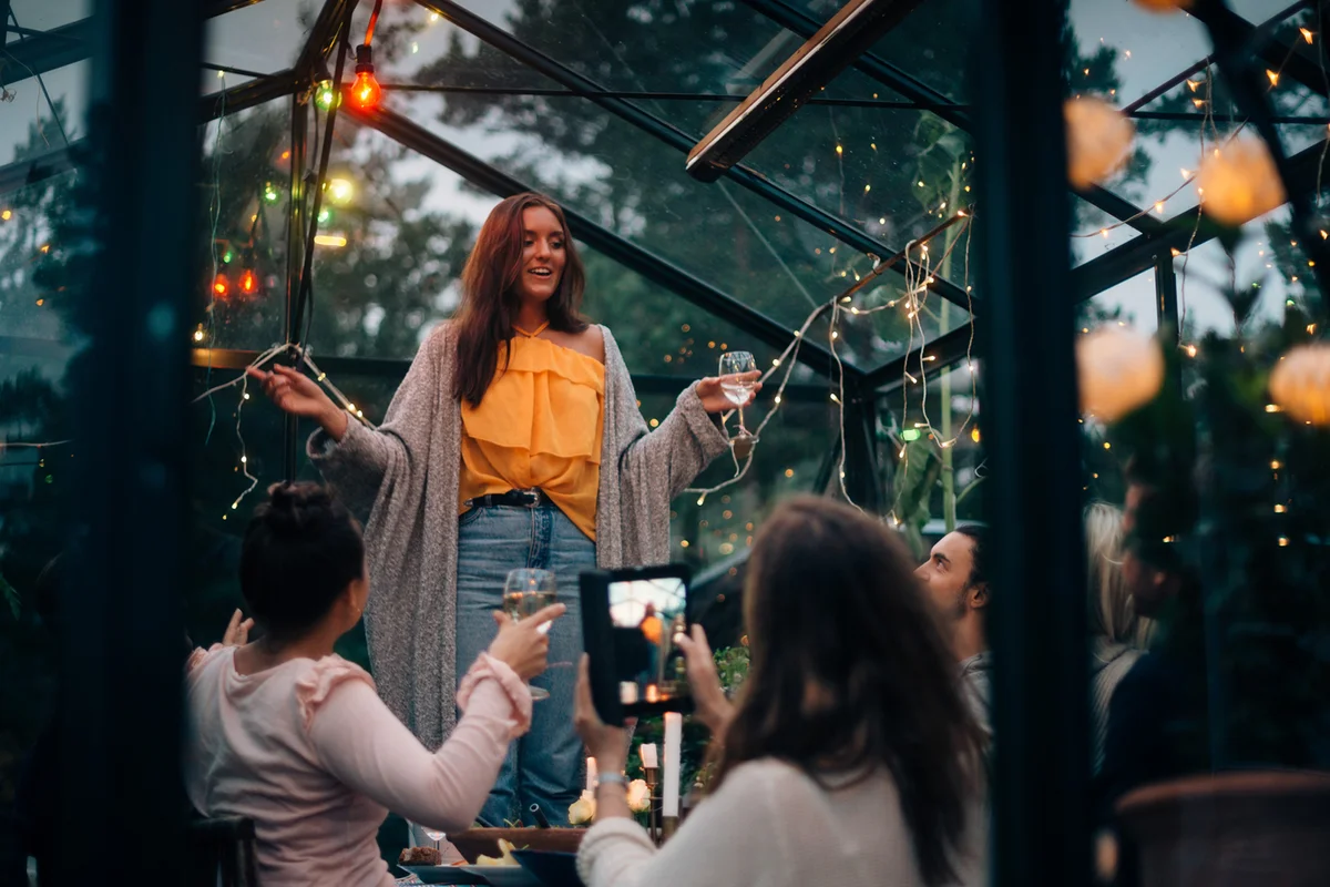 Young woman standing while toasting for friends in glass cabin