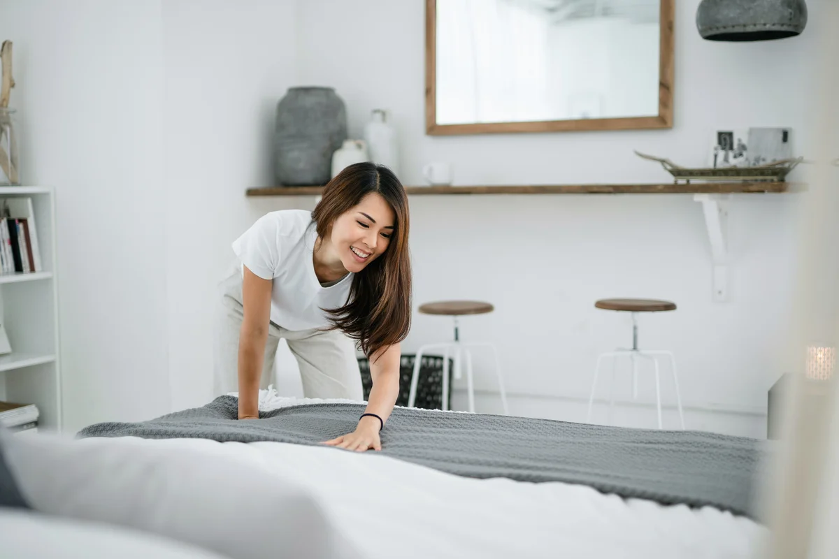 Woman making her bed and tidying her bedroom