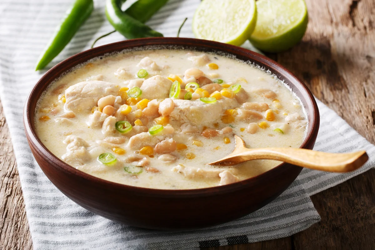 Homemade white chili chicken with beans, lime and corn close-up