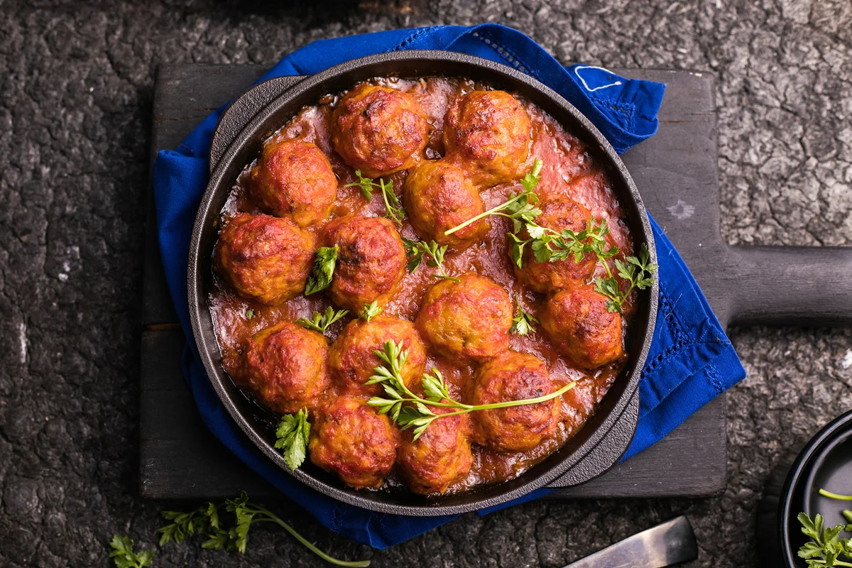 Meatballs with tomato sauce in a frying pan on a black background.