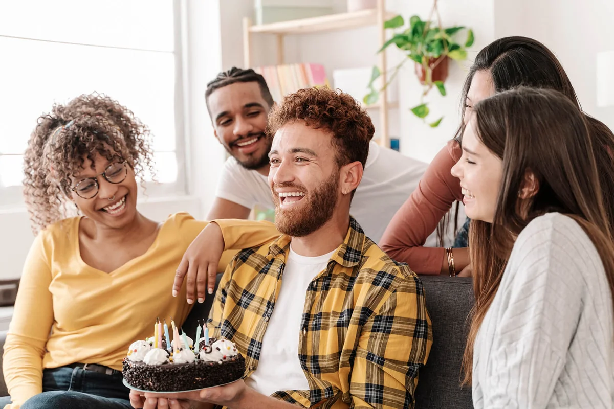 A happy young man with a birthday cake celebrating with his friends in the living room
