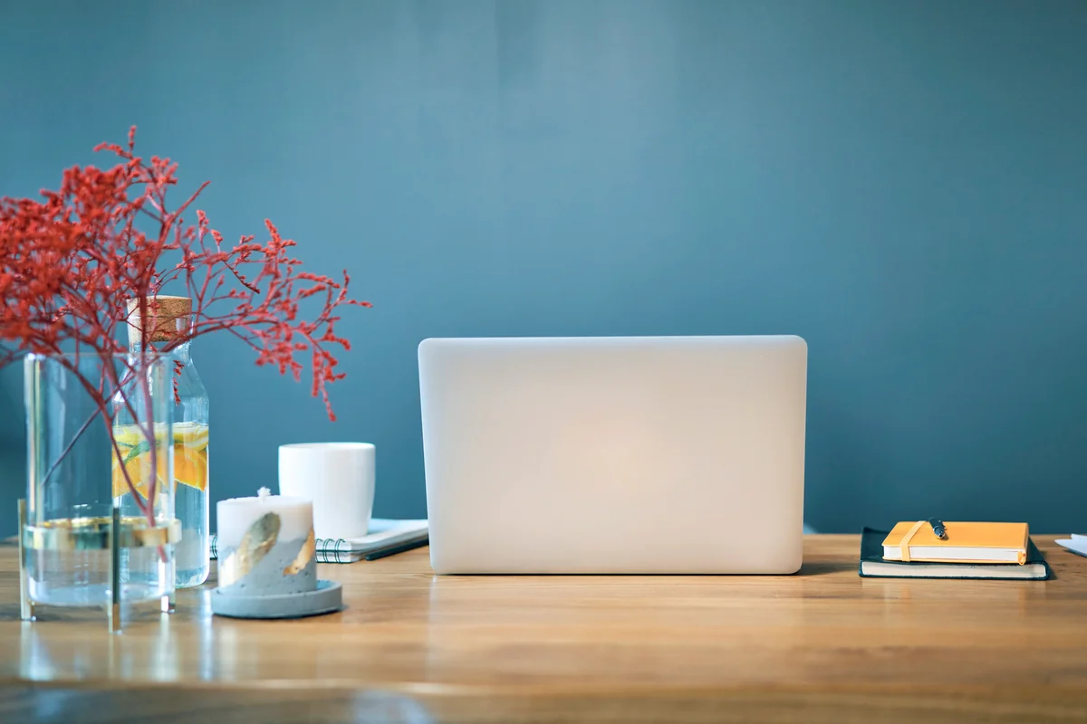 Laptop with diaries and decorations on desk against blue wall in home office