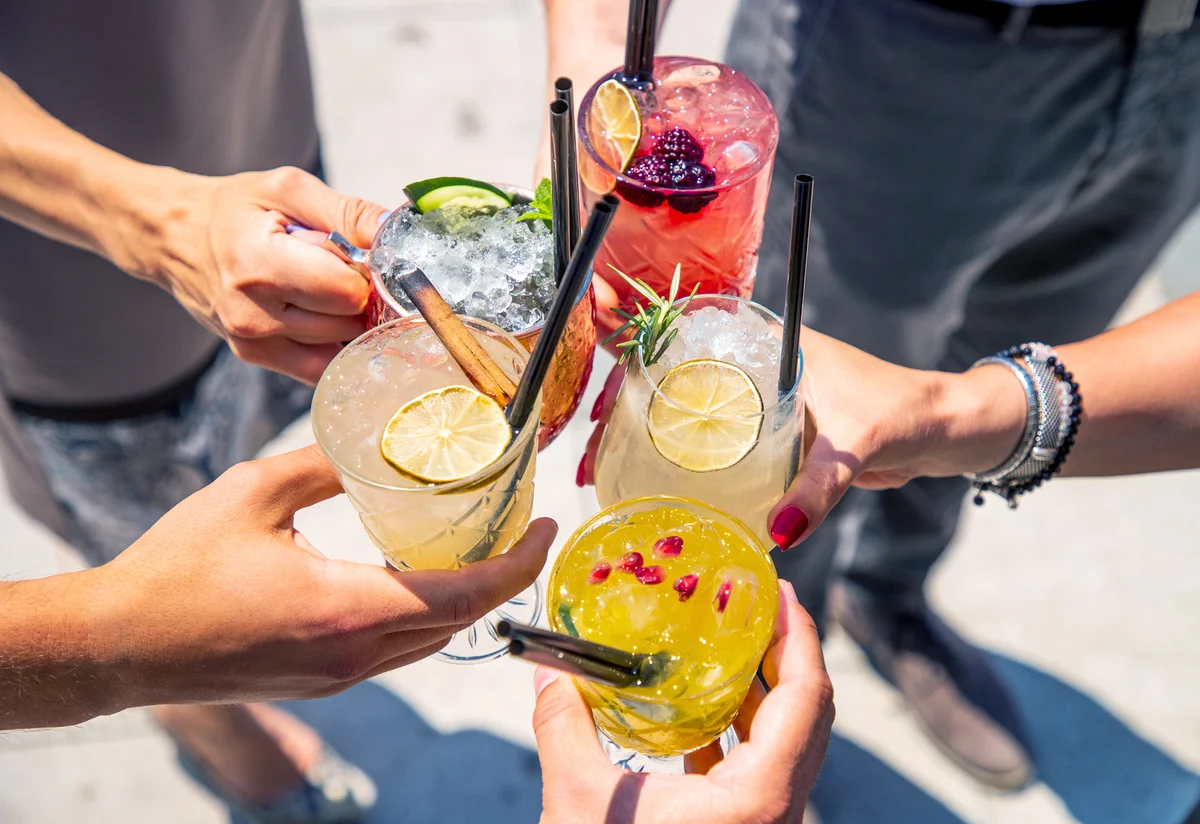 Five hands holding lemon mocktails in celebratory toast