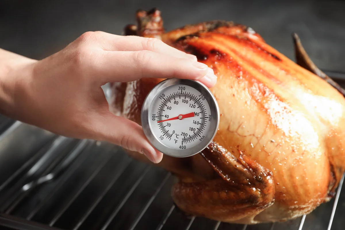 Woman measuring temperature of whole roasted turkey with meat thermometer | Photo 151358439 © Chernetskaya | Dreamstime.com