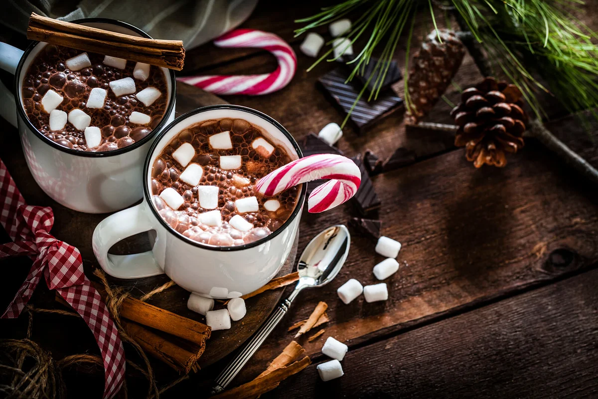 Two homemade hot chocolate mugs with marshmallows on rustic wooden Christmas table