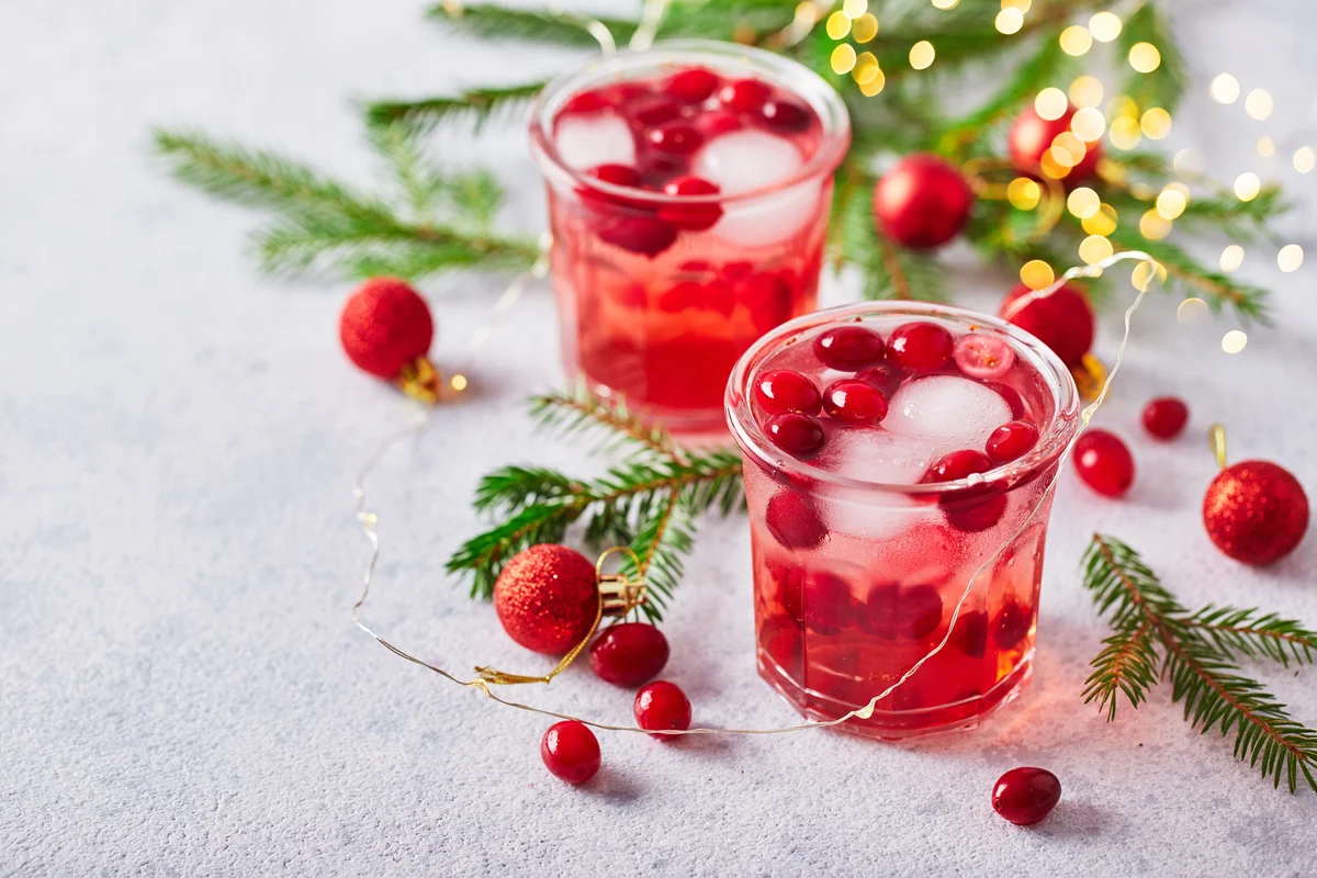 Alcoholic cocktail with cranberries with fir branches and glowing garland for christmas