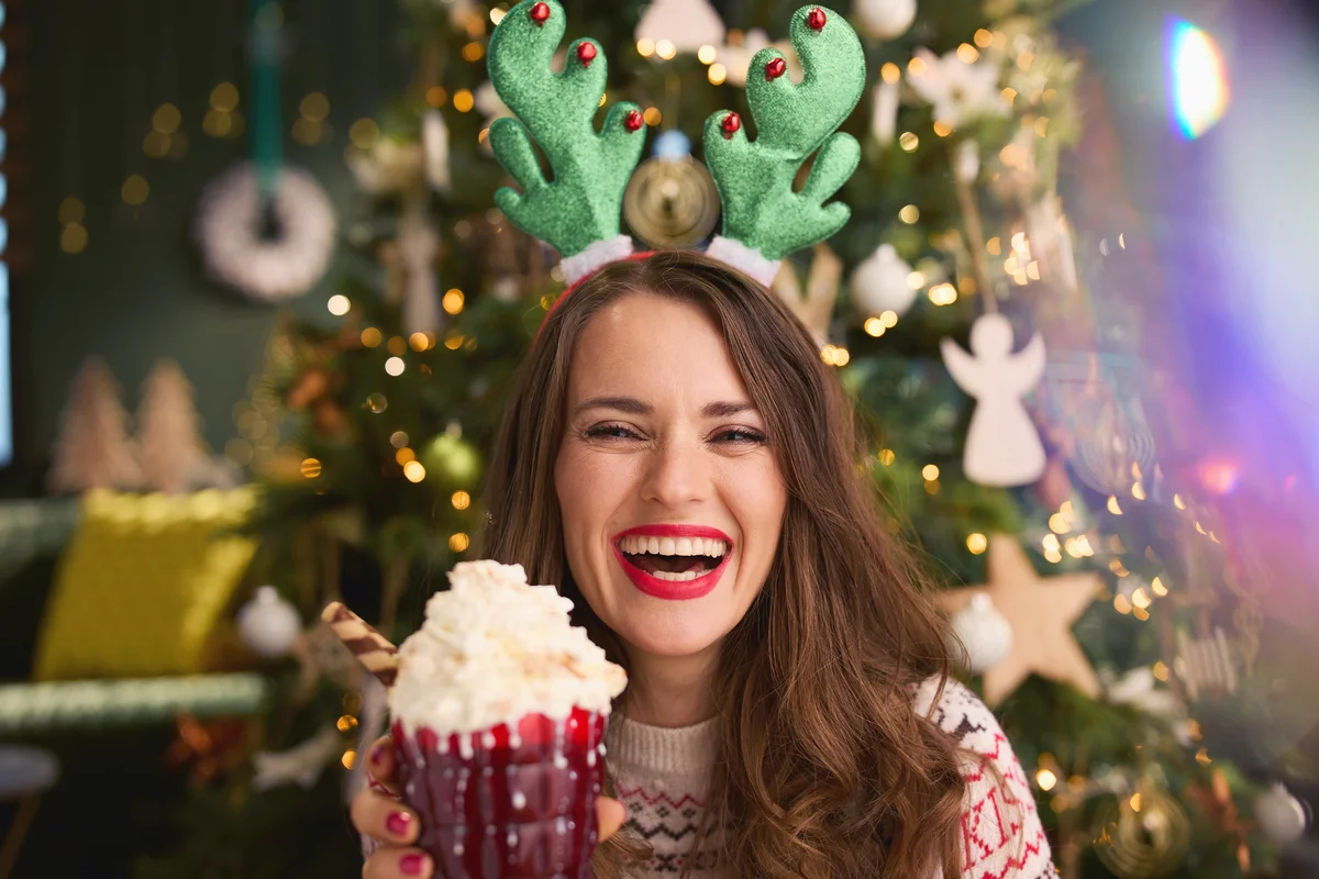 Woman holding festive hot chocolate cocktail near Christmas tree