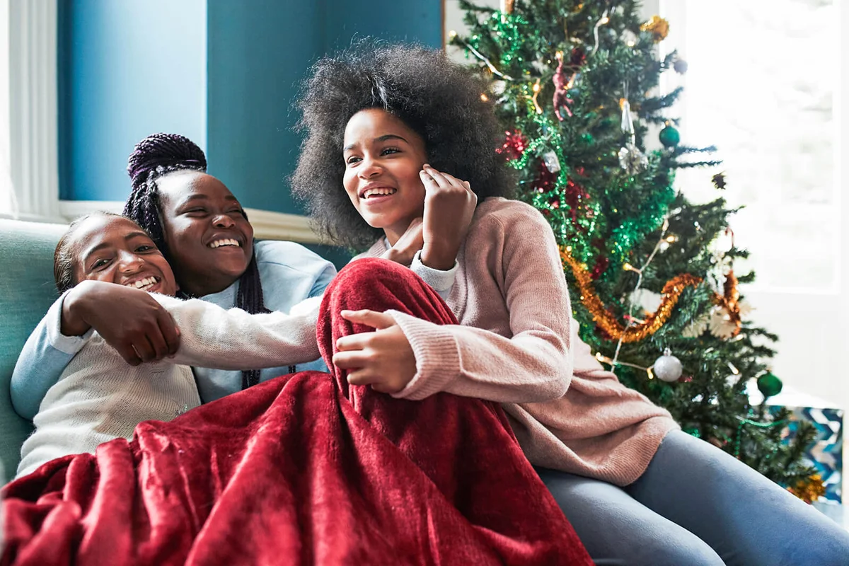Happy sisters embracing while sitting on sofa by Christmas tree at home