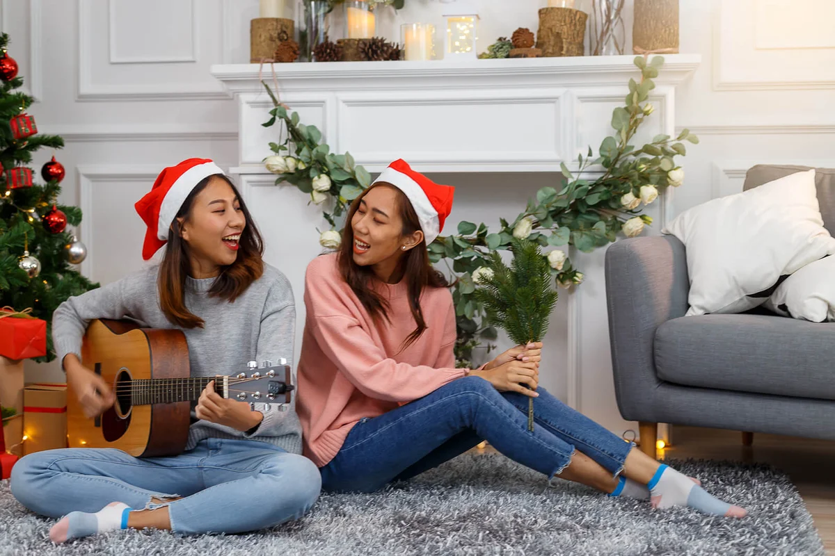 women in sweater singing and playing on acoustic guitar next to a Christmas tree