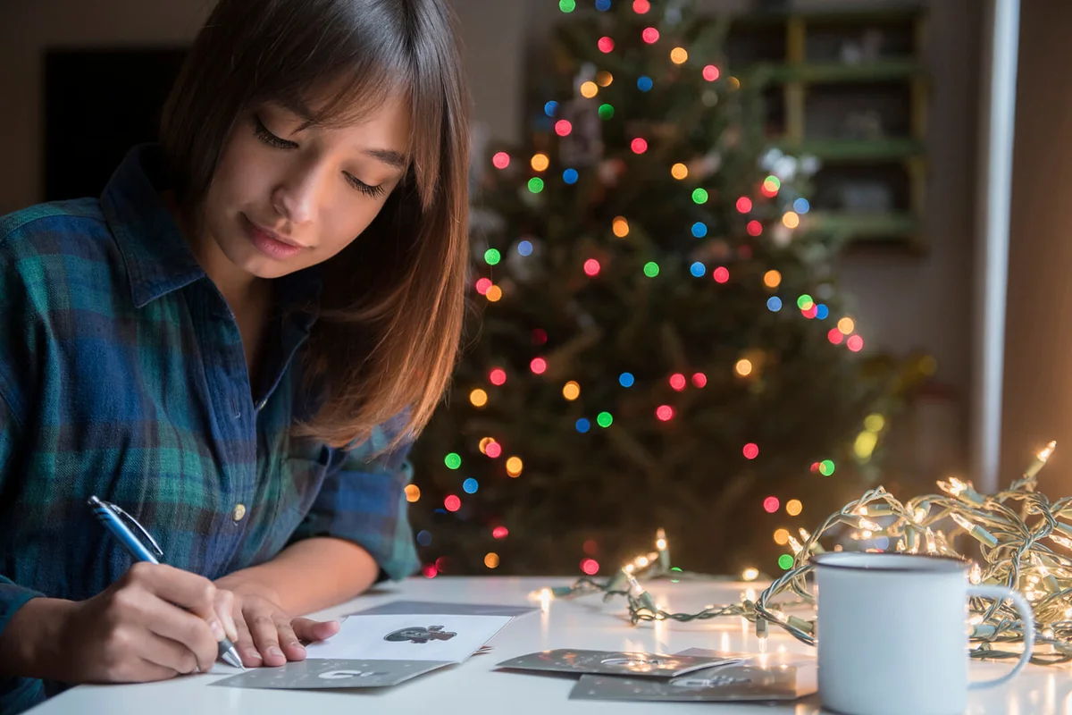woman writing on card near Christmas tree