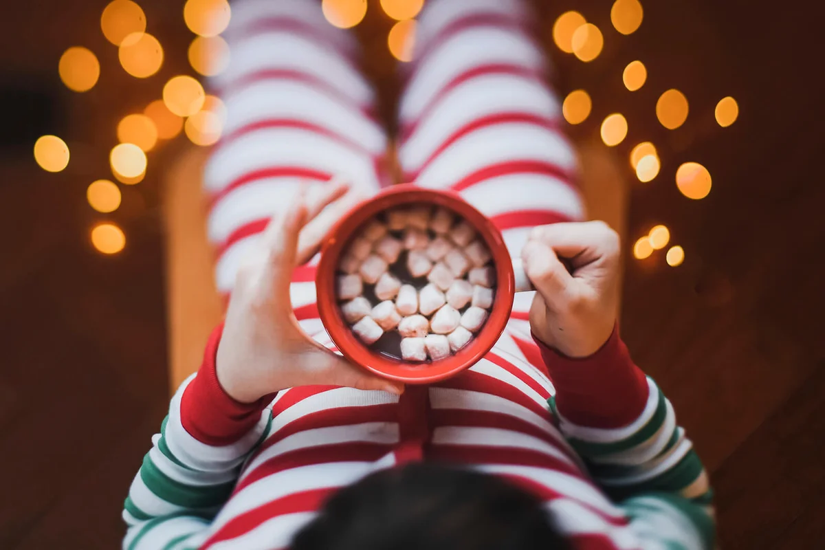 Child wearing Christmas pjs holds cup of hot cocoa with marshmalows