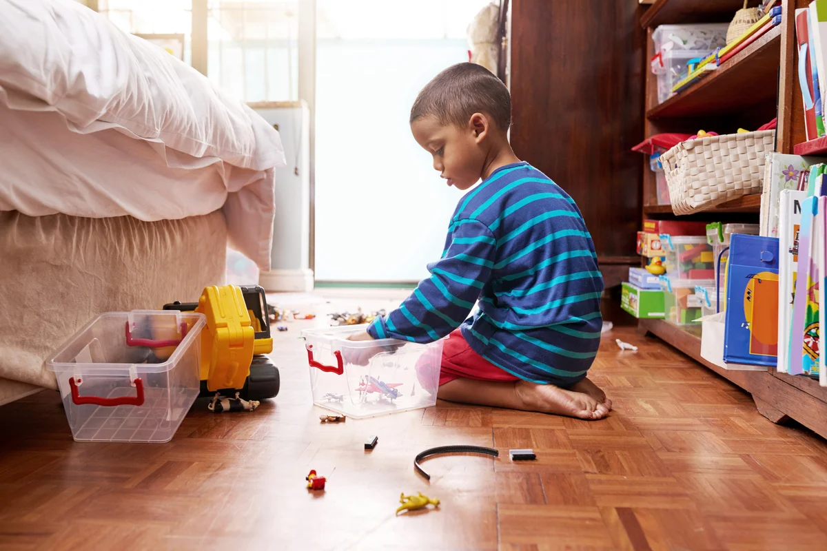 Young boy sitting on the floor picking up his toys
