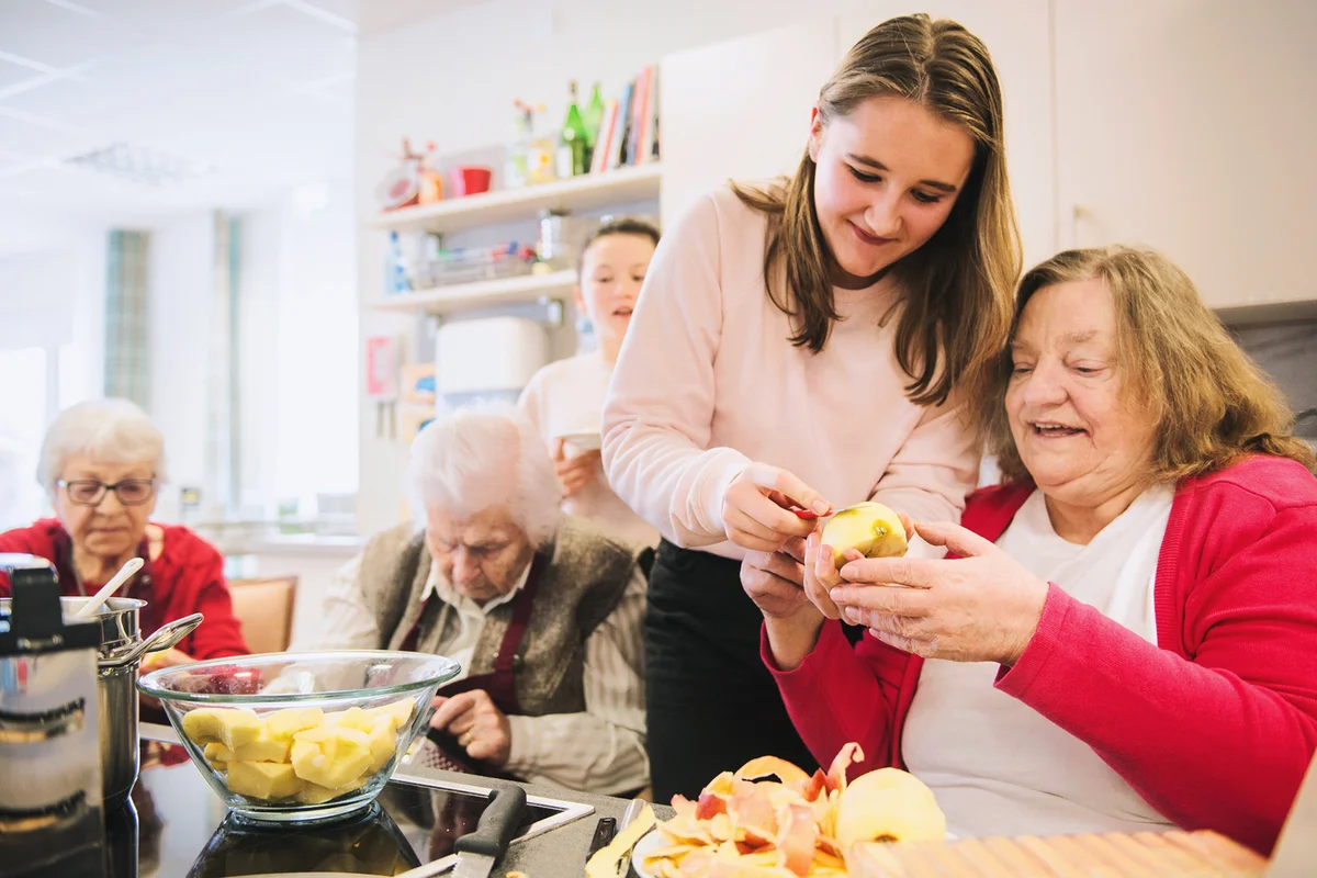 Senior woman with girl cutting apple at rest home