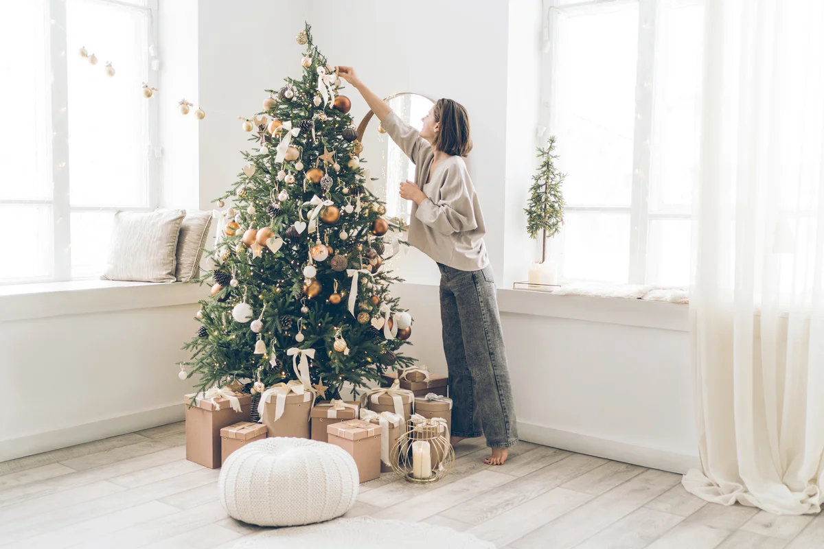 Young woman decorating Christmas tree in minimalist light interior