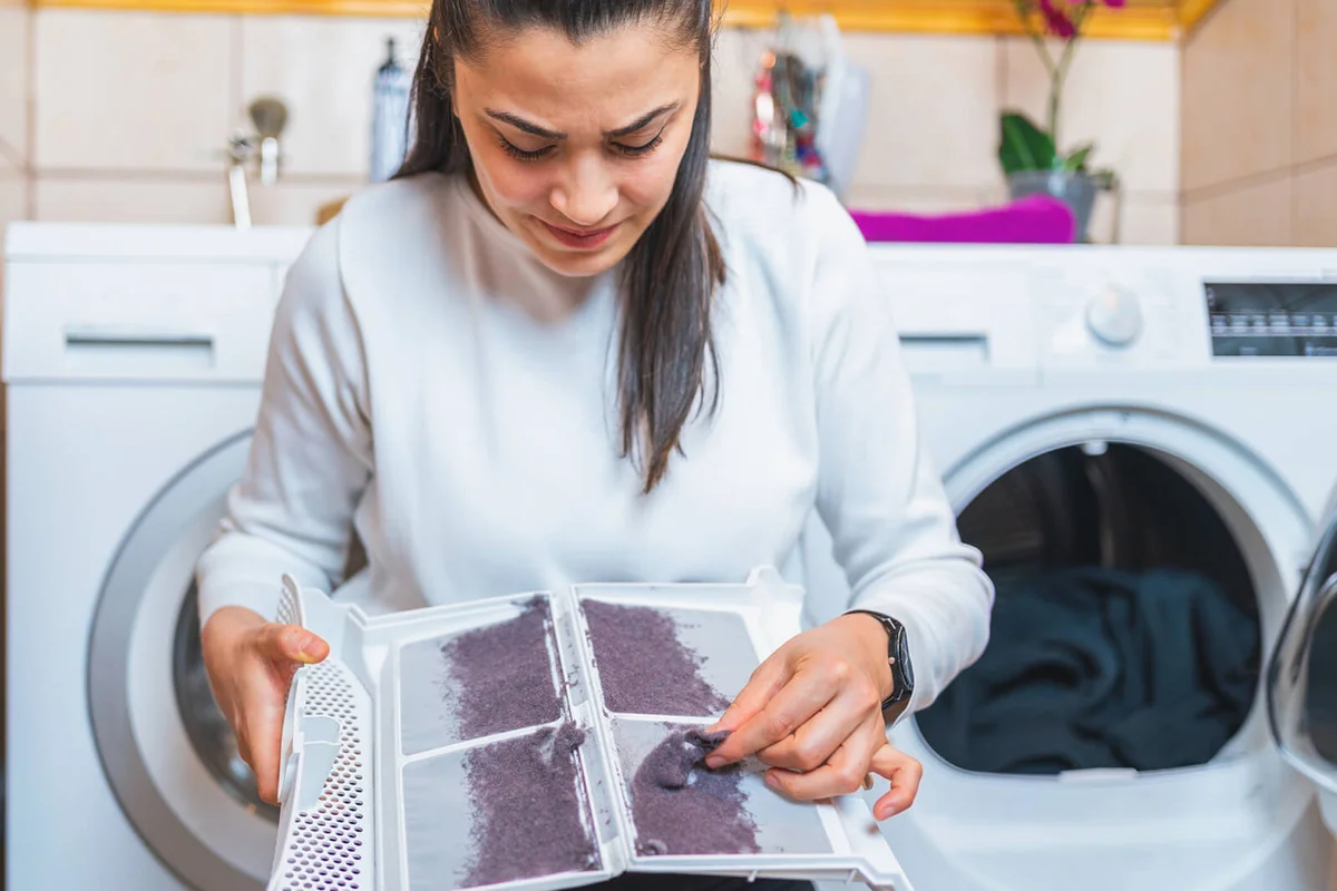 woman is removing lint from fluff dust filter of the tumble dryer