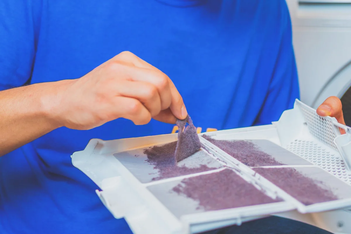 man is removing lint from fluff dust filter of the tumble dryer