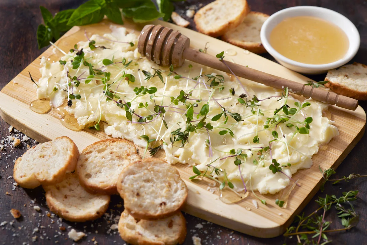 Butter Board with Fresh Herbs, Micro Greens, Organic Honey and Toasted Baguette Slices on a Bamboo Cutting Board