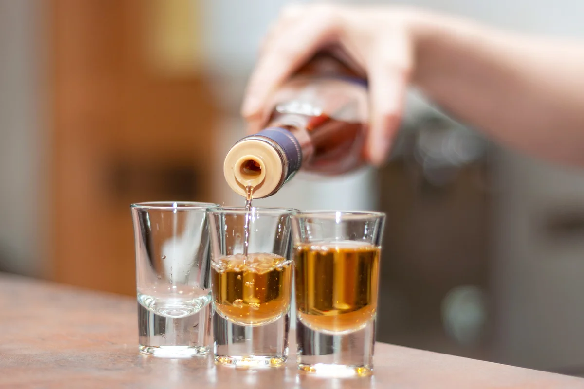 Hand pouring rum in shot glasses on table