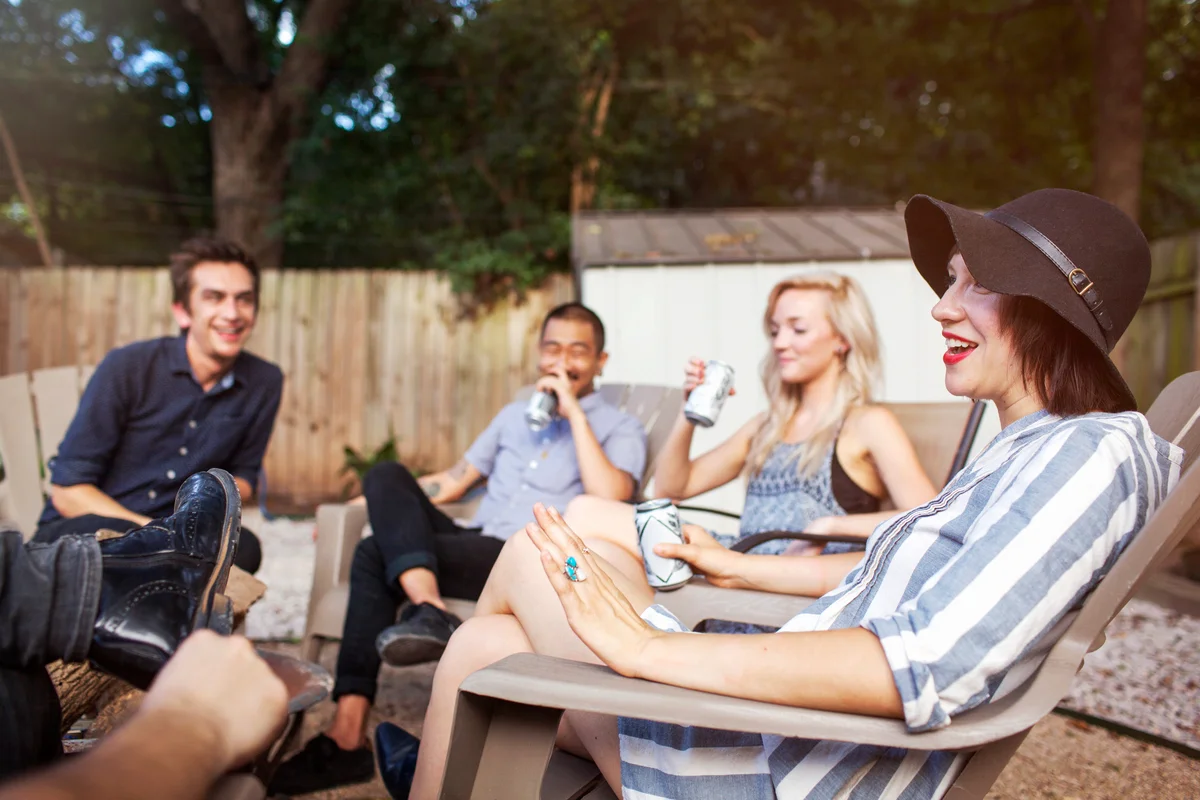 Friends talking and drinking while sitting on chairs in yard