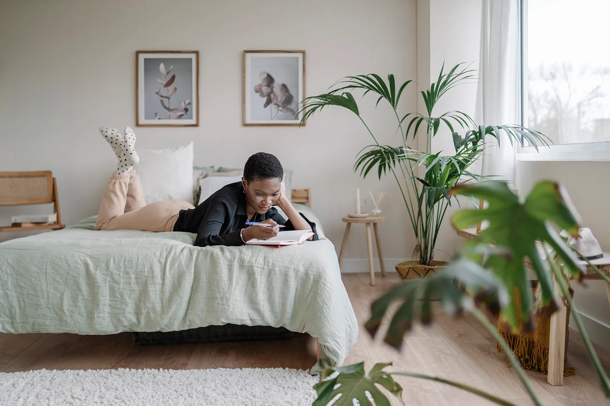 woman writing in a notebook while laying on a comfortable bed
