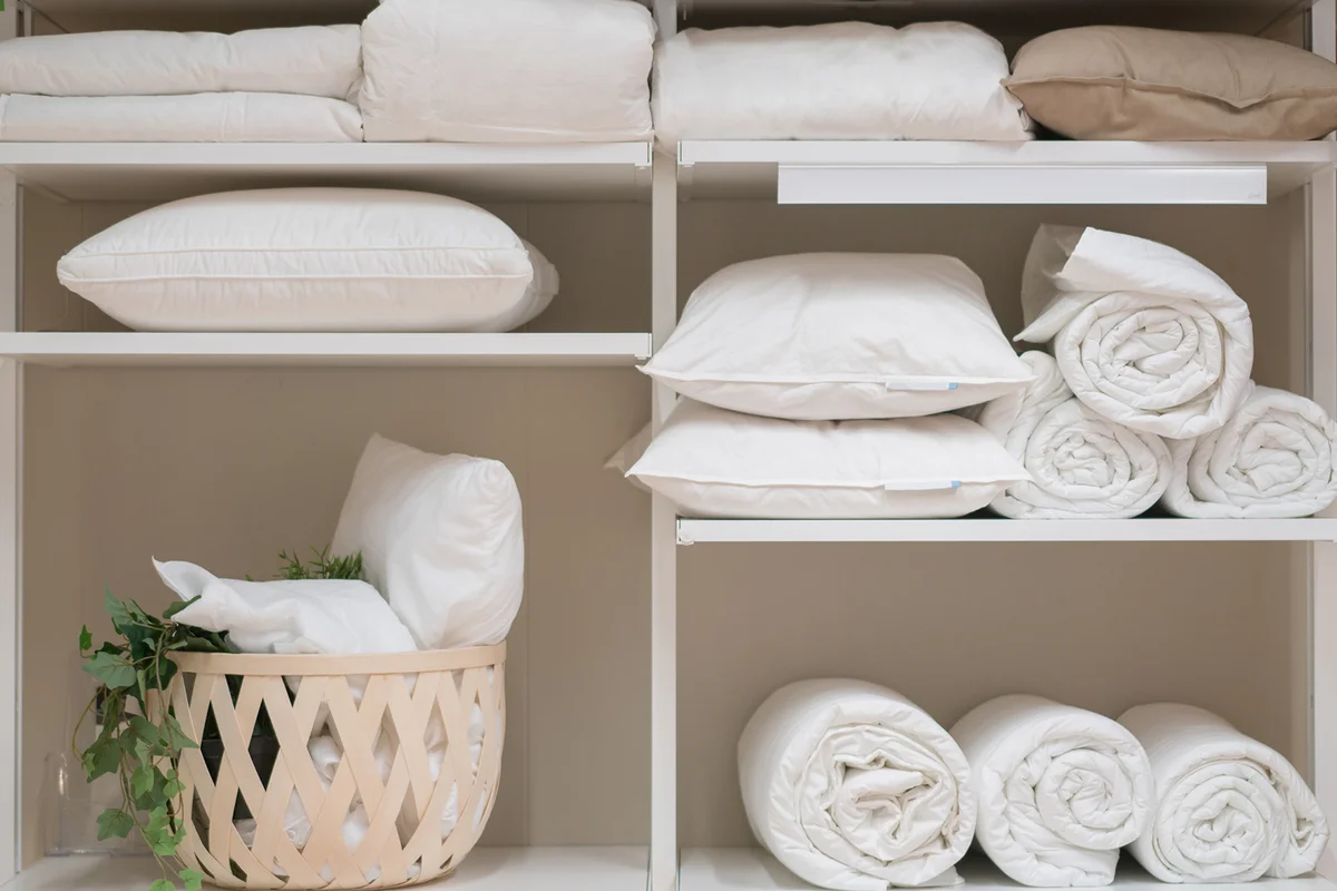 Various household items such as pillows and quilts standing in the white cupboard