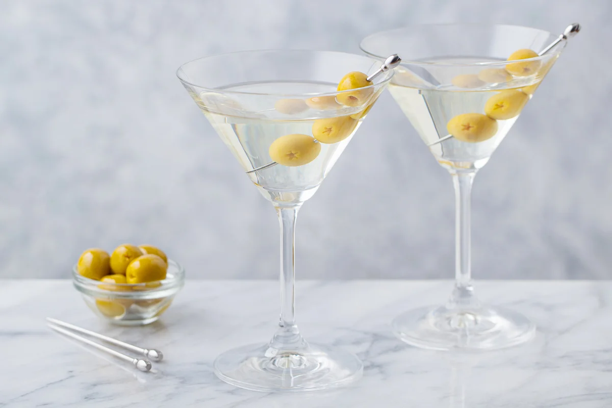 Gin martini cocktails with green olives on marble table