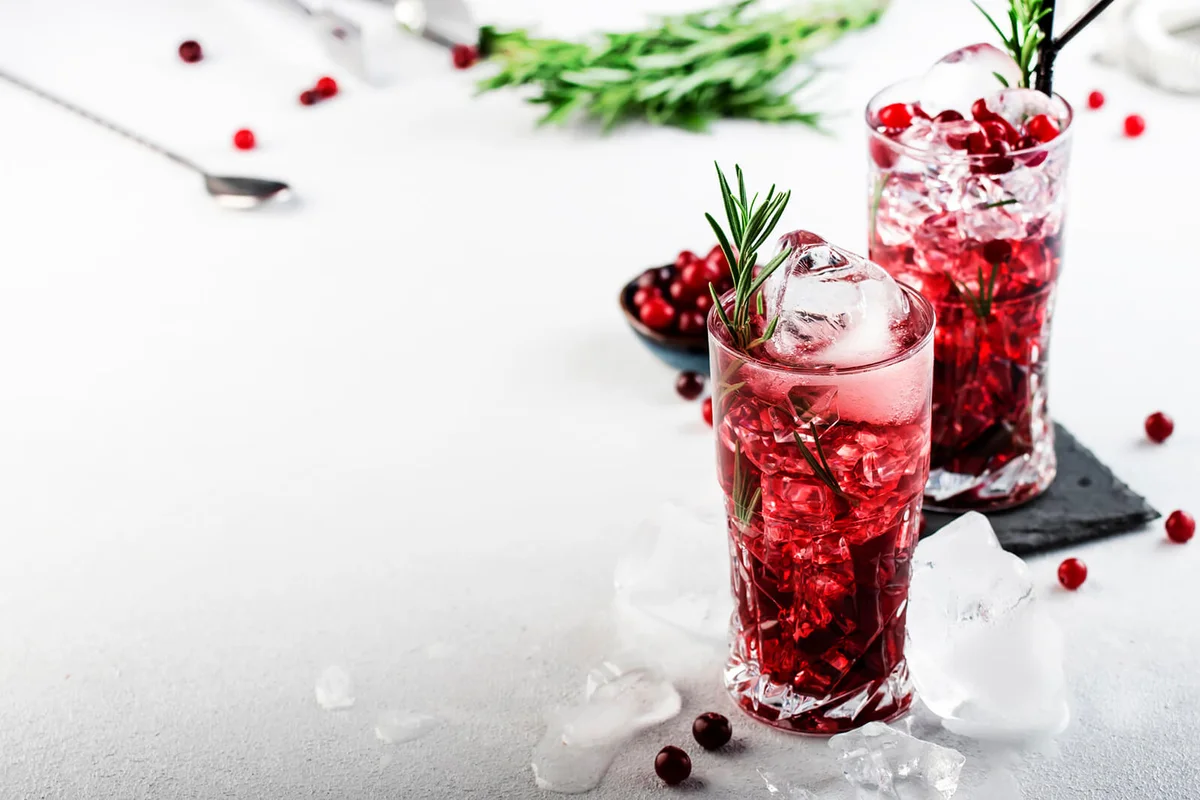 Cranberry cocktail with ice, rosemary and berries in highball glass