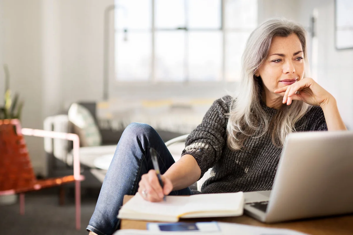 Mature woman writing in diary while working at home