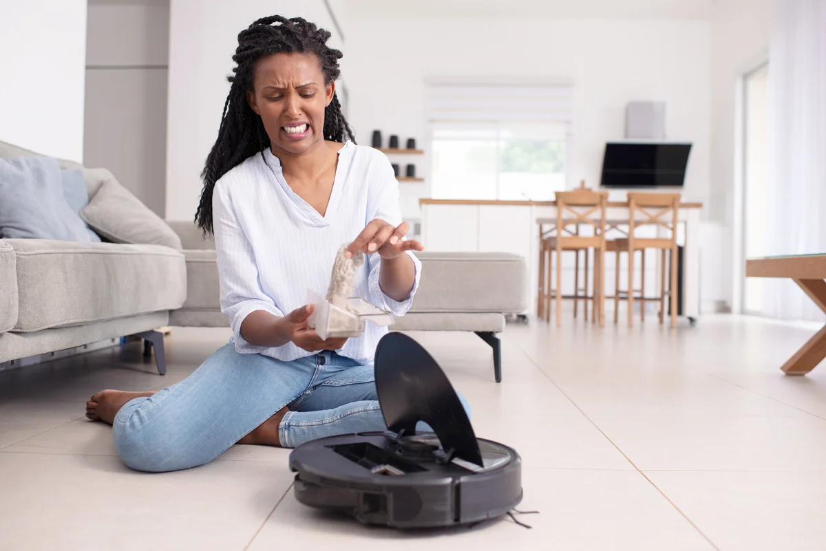 Woman looking disgusted showing clogged filter and full dust box of the robot vacuum cleaner