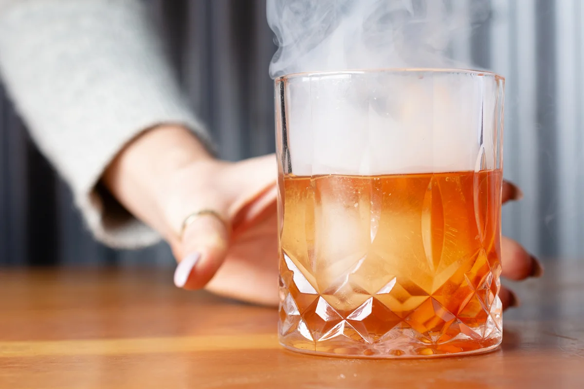 Hand holding smoked cocktail on table