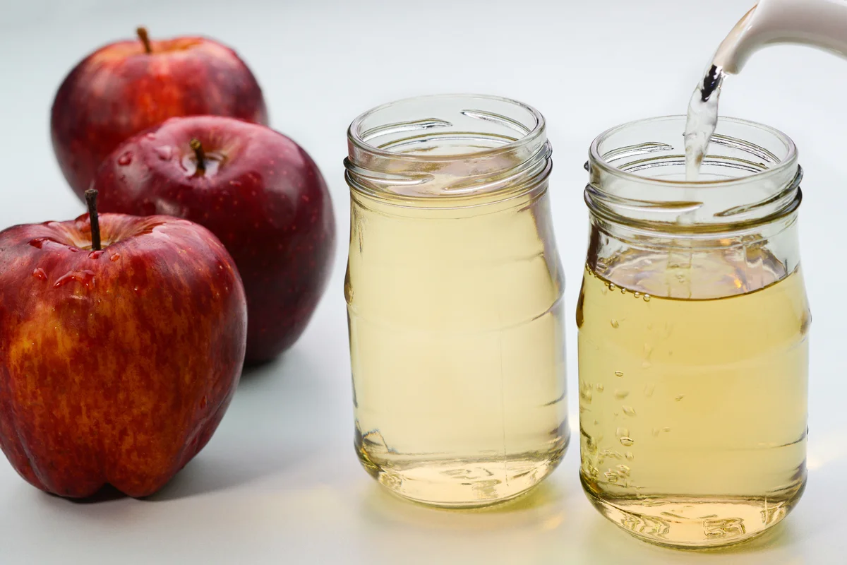 Serving apple cider vinegar in glass bottles with red apples in the background.